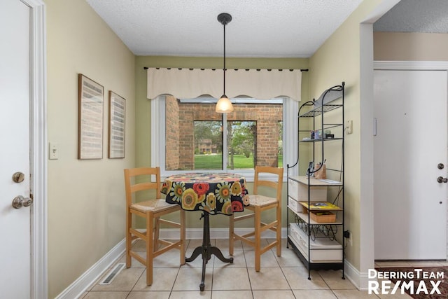 tiled dining space with baseboards, a textured ceiling, and visible vents