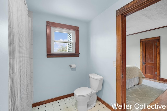 ensuite bathroom with toilet, tile patterned floors, a shower with shower curtain, baseboards, and ensuite bathroom