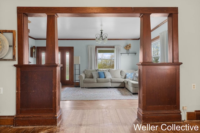 living area with wood-type flooring, ornamental molding, decorative columns, and an inviting chandelier