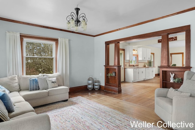 living room featuring baseboards, light wood-style flooring, crown molding, and a chandelier
