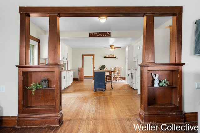 hallway with baseboards, decorative columns, and light wood finished floors