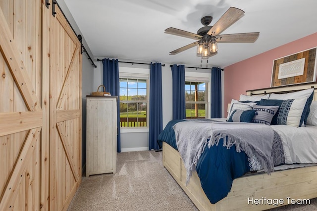 carpeted bedroom with baseboards, a barn door, and a ceiling fan