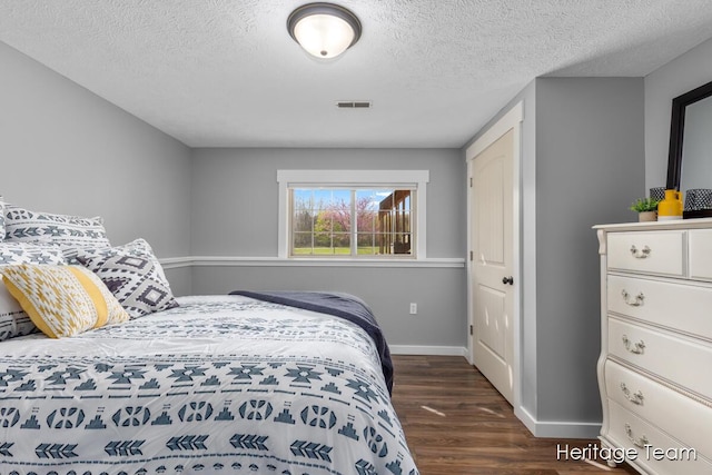 bedroom with baseboards, dark wood finished floors, a textured ceiling, and visible vents