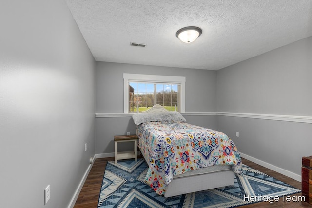 bedroom with a textured ceiling, baseboards, visible vents, and wood finished floors