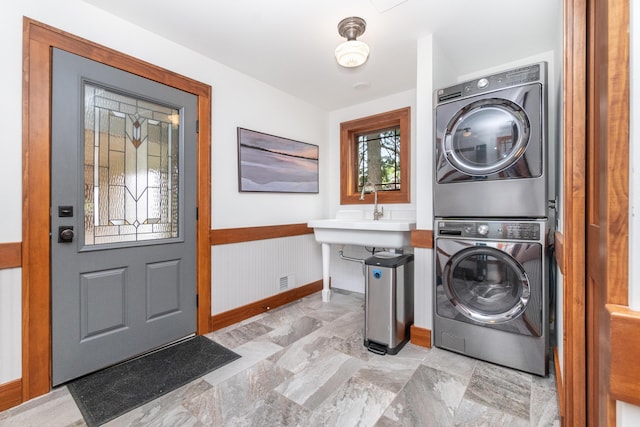 laundry area featuring a sink, baseboards, stacked washer / drying machine, and wainscoting