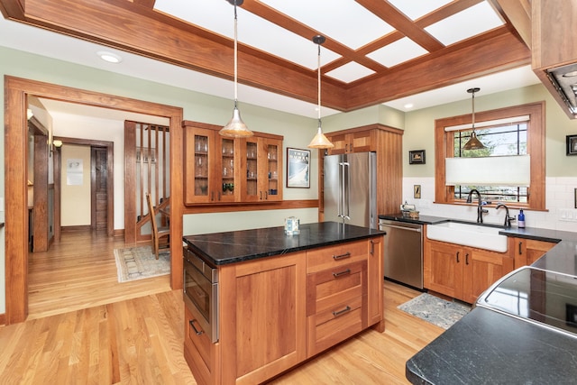 kitchen with stainless steel appliances, glass insert cabinets, a sink, and light wood-style flooring