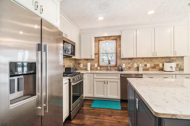 kitchen featuring a textured ceiling, a sink, white cabinets, dark wood-style floors, and stainless steel appliances
