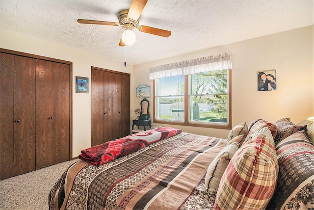 carpeted bedroom with a ceiling fan, a textured ceiling, and two closets