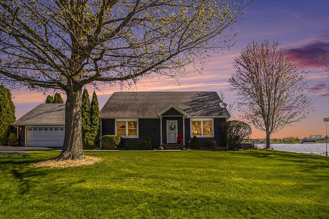 view of front facade with a lawn, a water view, an attached garage, and driveway