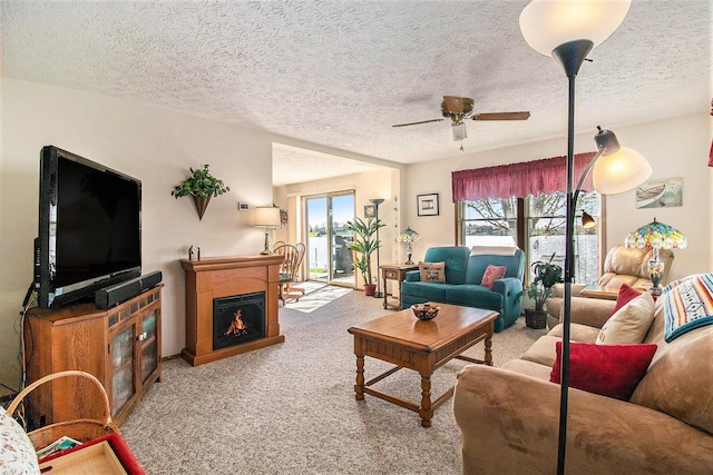 carpeted living room with plenty of natural light, a textured ceiling, ceiling fan, and a warm lit fireplace