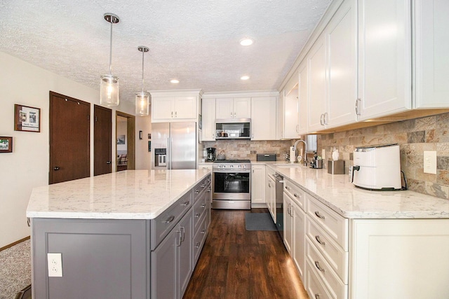 kitchen featuring dark wood-style flooring, appliances with stainless steel finishes, a sink, gray cabinets, and a center island
