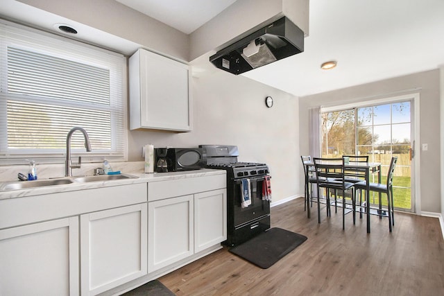 kitchen with white cabinets, a sink, black range with gas cooktop, light wood-type flooring, and under cabinet range hood