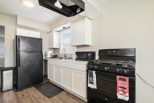 kitchen with ventilation hood, a sink, light wood-style floors, white cabinetry, and black appliances
