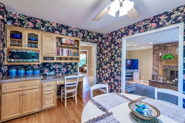 dining space featuring built in desk, a fireplace, a ceiling fan, wallpapered walls, and light wood-type flooring