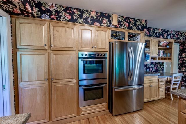 kitchen featuring light brown cabinetry, wallpapered walls, appliances with stainless steel finishes, and open shelves