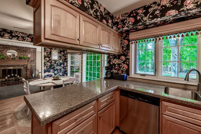 kitchen featuring stainless steel dishwasher, a peninsula, a brick fireplace, stone countertops, and a sink