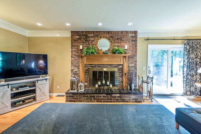 living room with crown molding, recessed lighting, a brick fireplace, and wood finished floors