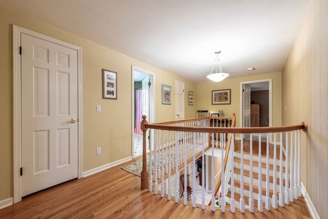 corridor with baseboards, wood finished floors, and an upstairs landing
