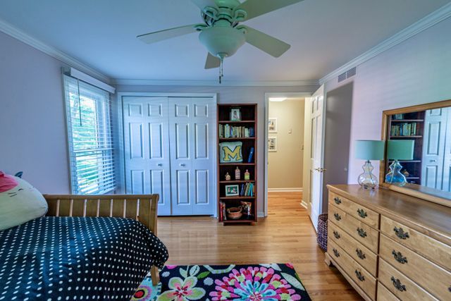 bedroom featuring visible vents, ornamental molding, light wood-style flooring, and a ceiling fan