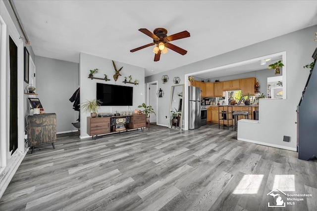 living room with light wood-style floors, baseboards, and ceiling fan