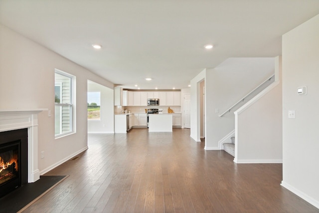 unfurnished living room with a glass covered fireplace, baseboards, stairway, dark wood-type flooring, and recessed lighting