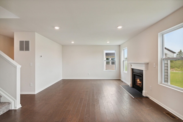 unfurnished living room with a glass covered fireplace, stairs, dark wood-style floors, and visible vents