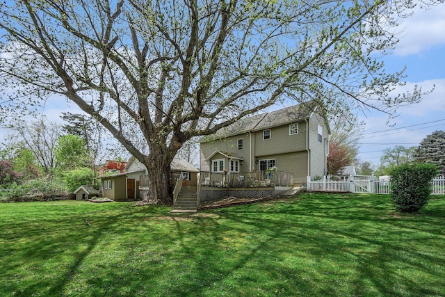 back of house featuring fence, a storage unit, a wooden deck, a lawn, and an outdoor structure
