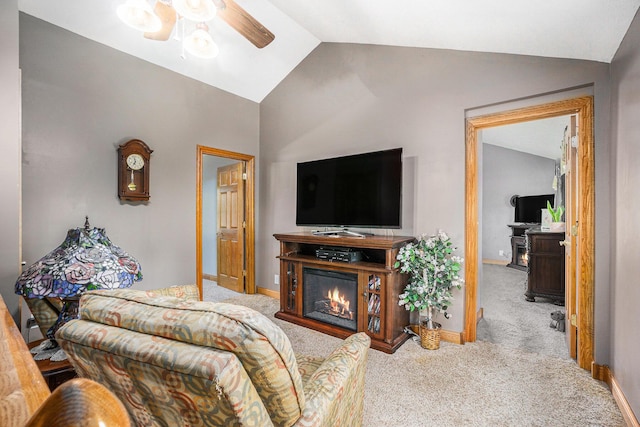 living area featuring a ceiling fan, carpet floors, baseboards, lofted ceiling, and a glass covered fireplace