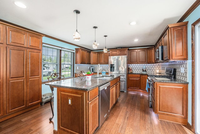 kitchen featuring appliances with stainless steel finishes, a sink, dark stone counters, backsplash, and dark wood-style floors