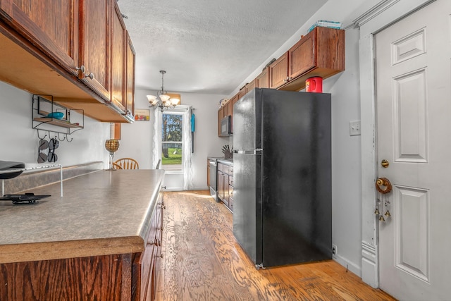 kitchen featuring a notable chandelier, a textured ceiling, brown cabinetry, light wood-style flooring, and freestanding refrigerator