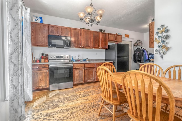 kitchen featuring light countertops, a textured ceiling, a chandelier, light wood finished floors, and black appliances