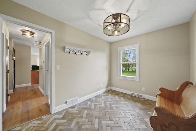 interior space featuring visible vents, a textured ceiling, baseboards, and a notable chandelier
