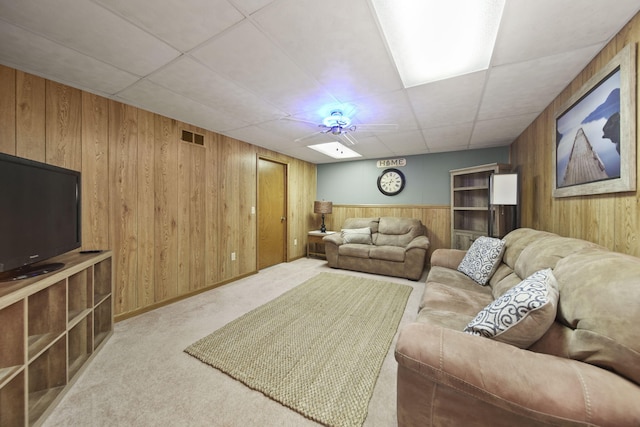 living area featuring carpet floors, wood walls, a drop ceiling, and visible vents