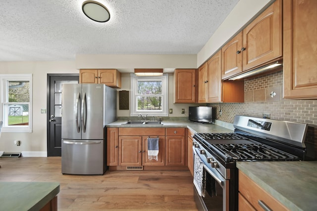 kitchen with a sink, appliances with stainless steel finishes, light wood-type flooring, and a textured ceiling
