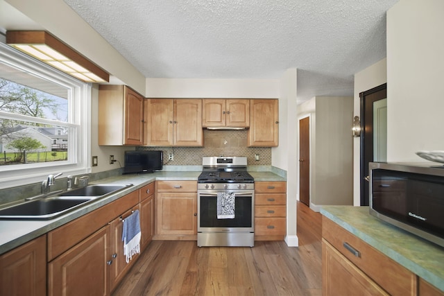 kitchen with wood finished floors, a textured ceiling, tasteful backsplash, a sink, and appliances with stainless steel finishes