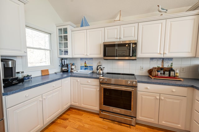 kitchen with stainless steel appliances, dark countertops, light wood-type flooring, and tasteful backsplash