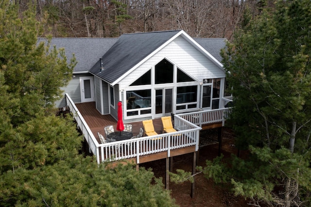 back of property with a shingled roof, a sunroom, and a deck