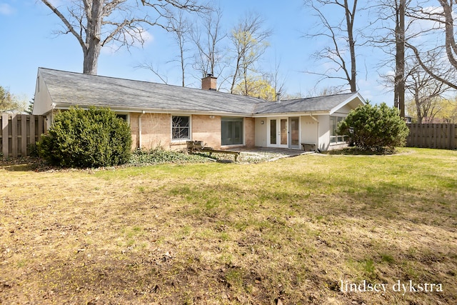 back of house with fence, brick siding, a chimney, french doors, and a yard