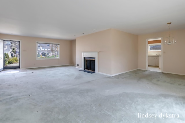 unfurnished living room featuring a fireplace with flush hearth, baseboards, light carpet, and a notable chandelier
