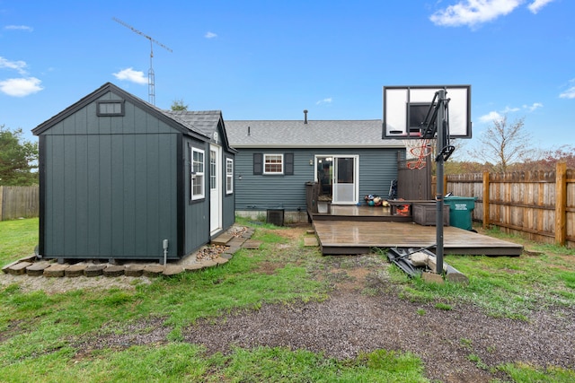 rear view of house with roof with shingles, a wooden deck, an outdoor structure, a fenced backyard, and a storage unit