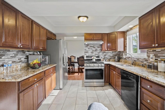 kitchen featuring light stone countertops, under cabinet range hood, tasteful backsplash, a sink, and appliances with stainless steel finishes