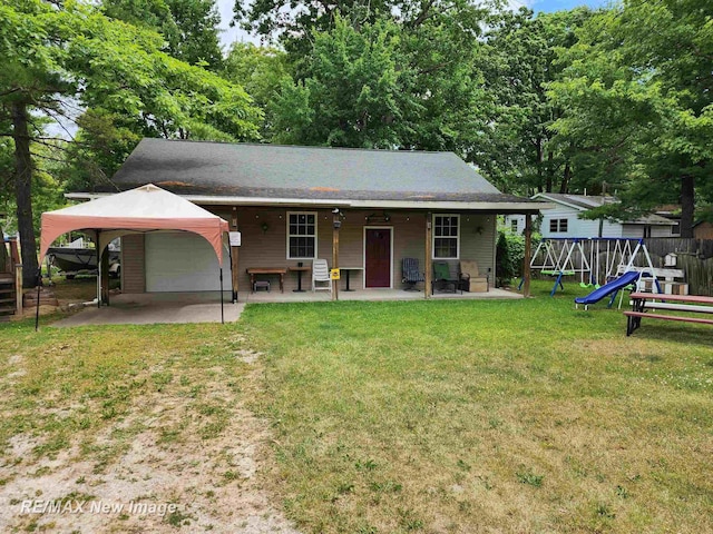 back of property with fence, a garage, a playground, a yard, and driveway