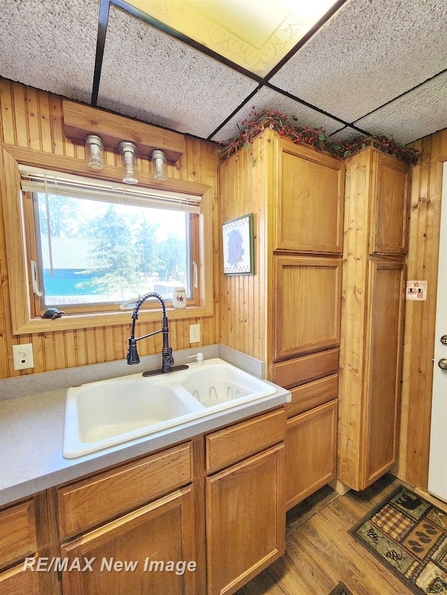 kitchen with brown cabinetry, wood finished floors, a sink, light countertops, and wooden walls