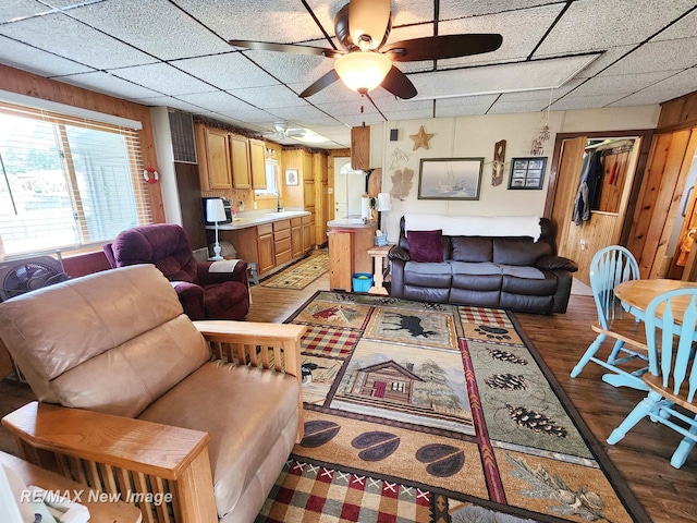 living room featuring wood walls, a ceiling fan, light wood-type flooring, and a paneled ceiling