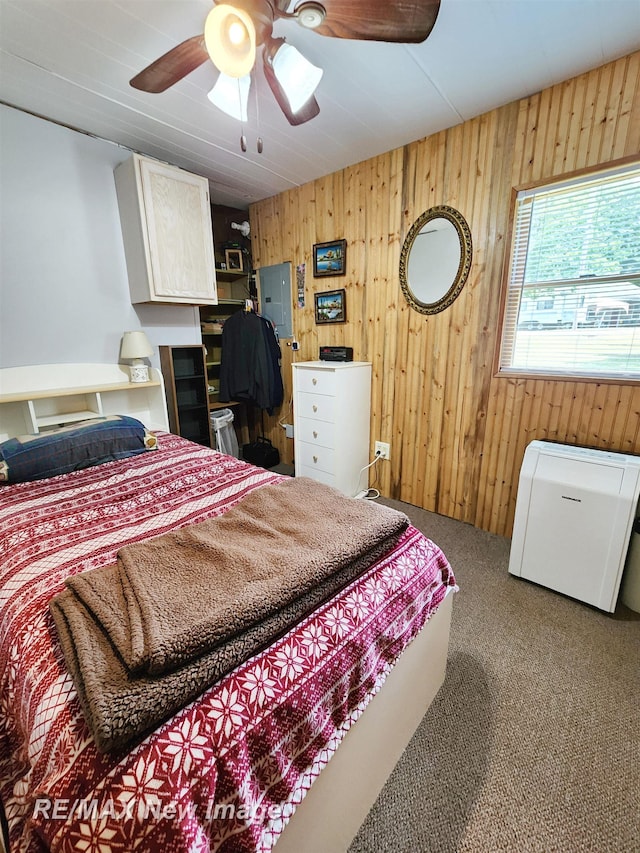 bedroom with carpet flooring, a ceiling fan, wood walls, and electric panel