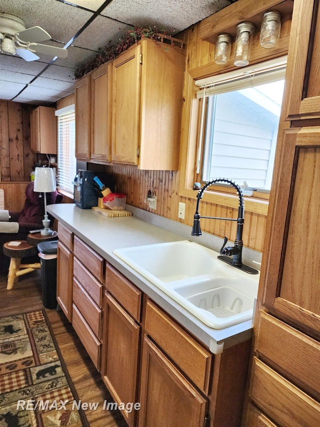 kitchen with wood walls, dark wood-style floors, light countertops, a paneled ceiling, and a sink