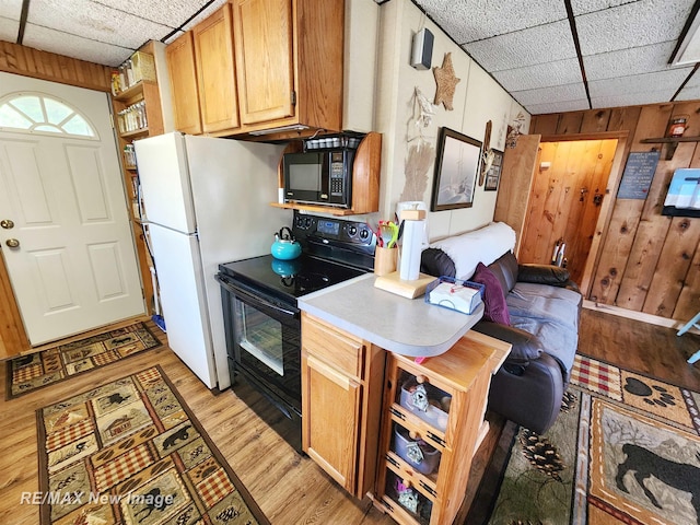 kitchen featuring light countertops, black appliances, wooden walls, light wood-style floors, and a drop ceiling