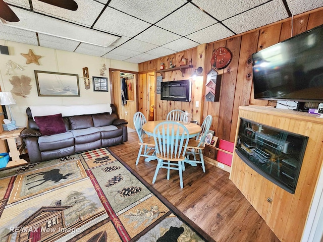living area with a drop ceiling, wood walls, and wood finished floors