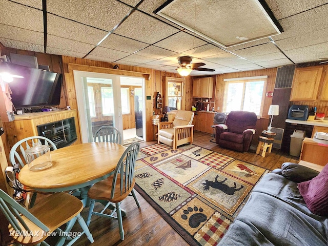 dining room featuring light wood-style floors, wood walls, a ceiling fan, and a drop ceiling