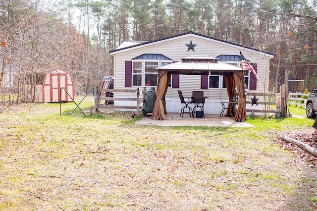 rear view of property with a gazebo, fence, an outdoor structure, a shed, and a patio